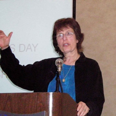 A person standing at a podium with her hand raised

Description automatically generated